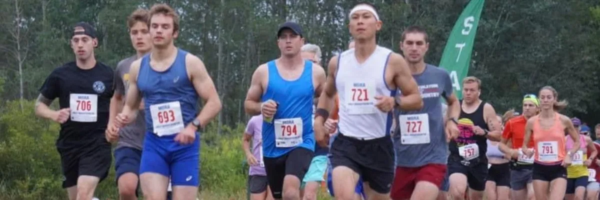 A group of runners in a race, with bib numbers visible, running forward.