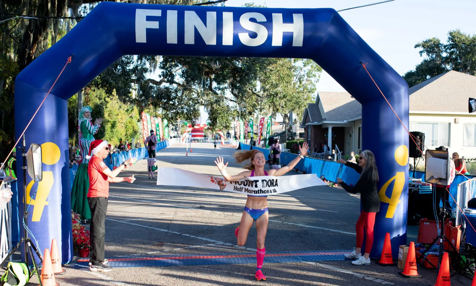 A female runner breaks the finish line tape with her arms raised in celebration at the Mount Dora Half Marathon & 5K.