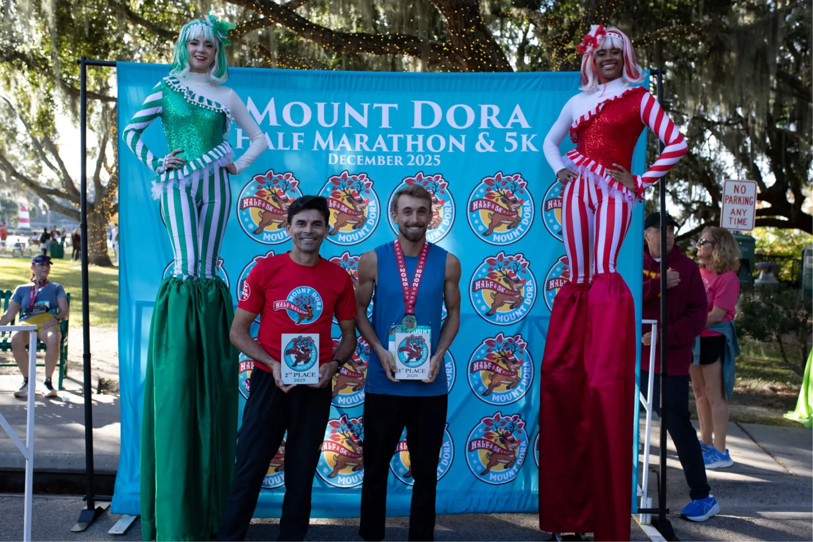 Runners receiving awards on a stage with costumed characters and a race backdrop.