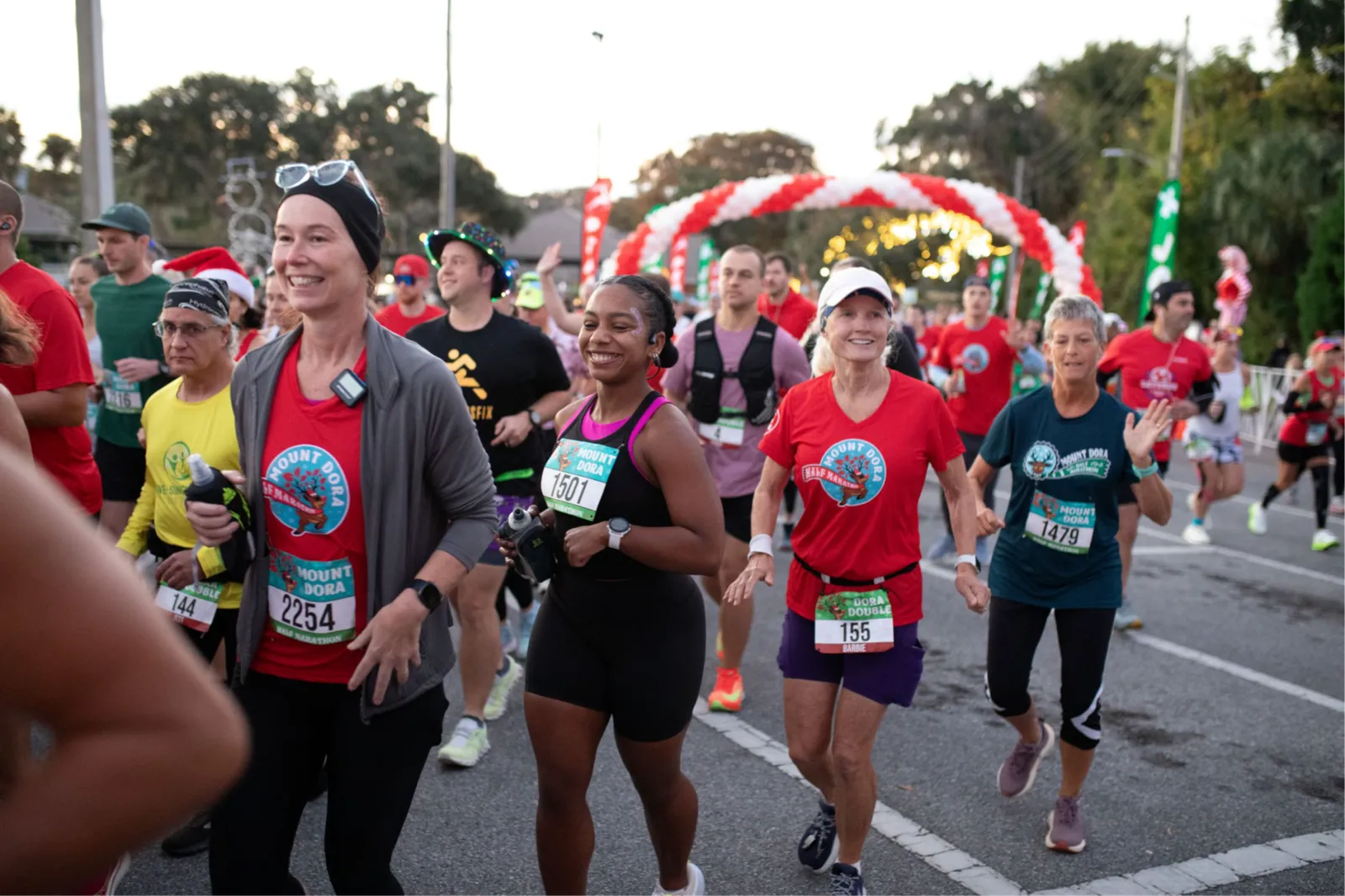 Runners smiling and participating in the Mount Dora Half Marathon, with a festive red and white archway in the background.