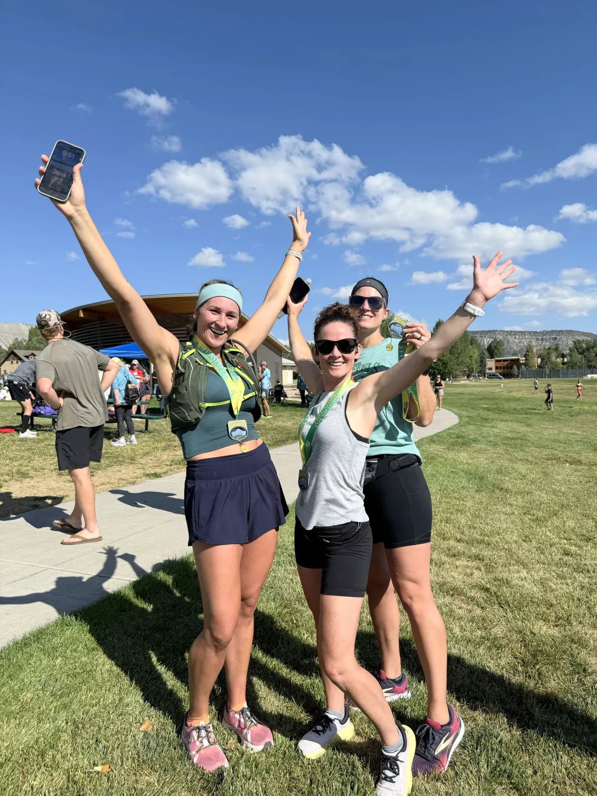 Three women smiling and celebrating with medals around their necks after a race.