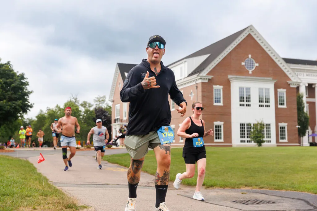 Runners on a road course with a large brick building in the background.