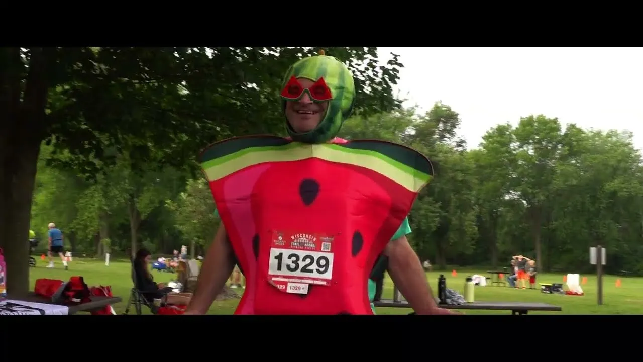 A runner wearing a watermelon costume with sunglasses and bib number 1329 at a race.