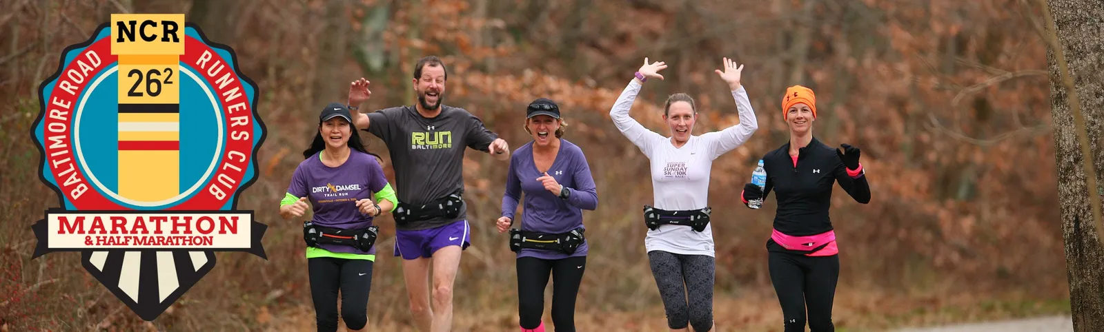 A group of runners smiling and waving as they run on a road, with race branding visible.