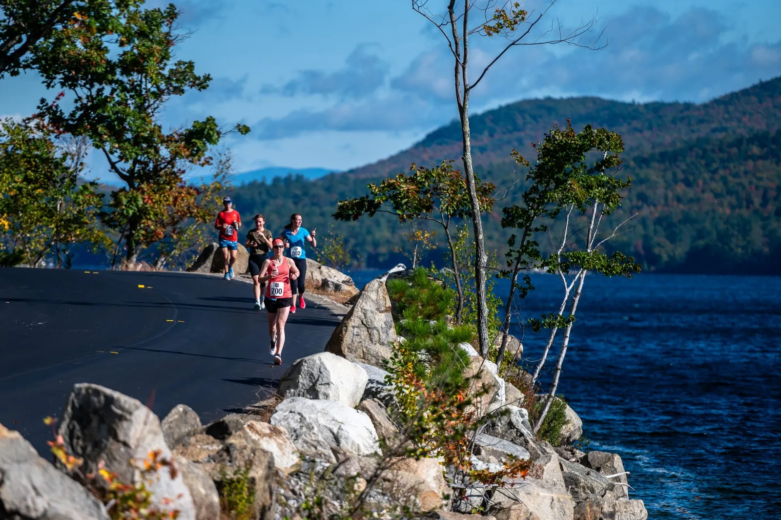 Runners on a road course with a lake and mountains in the background.