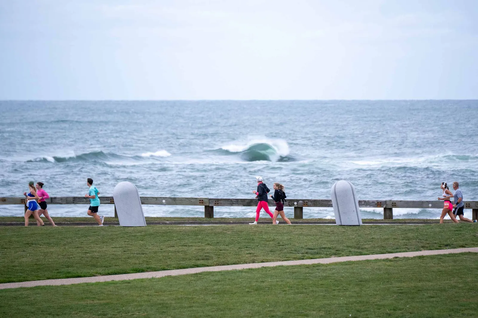 Runners on a path along the coast with waves in the background.