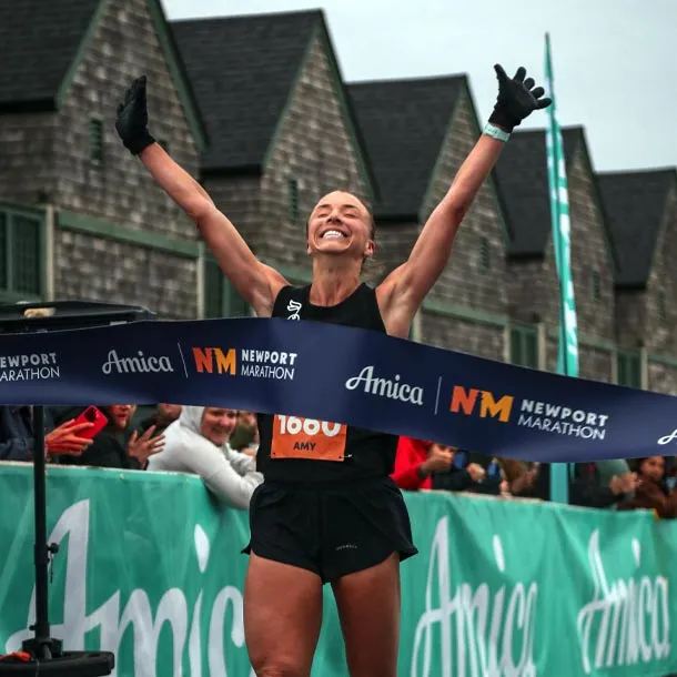 A female runner with her arms raised in victory crosses the finish line at the Newport Marathon.
