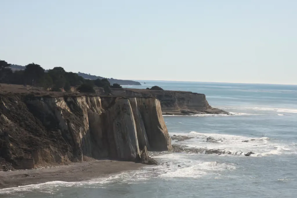 Coastal bluffs overlooking the ocean with waves crashing on the shore.