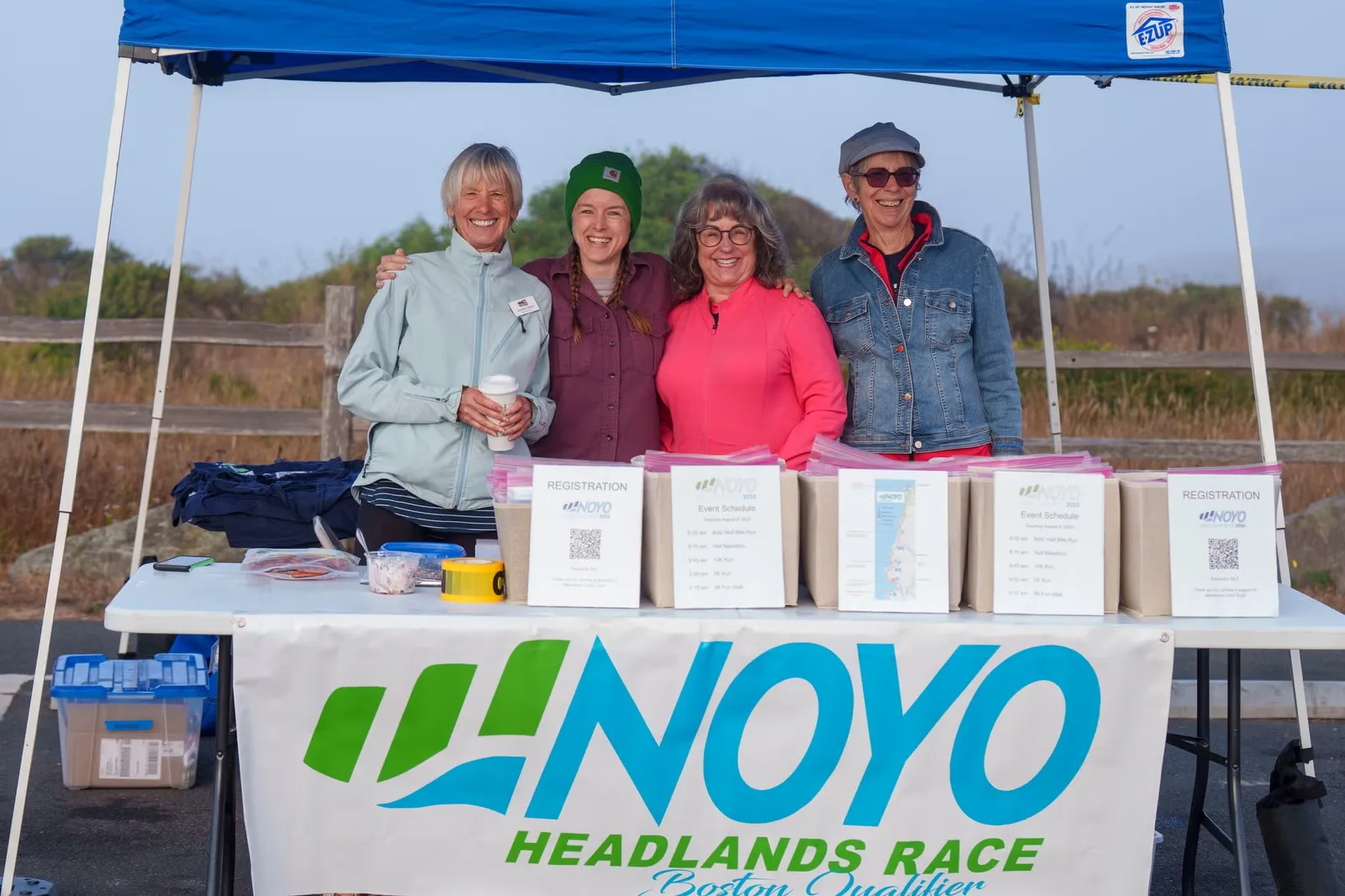 Four smiling people stand behind a registration table at the Noyo Headlands Race.