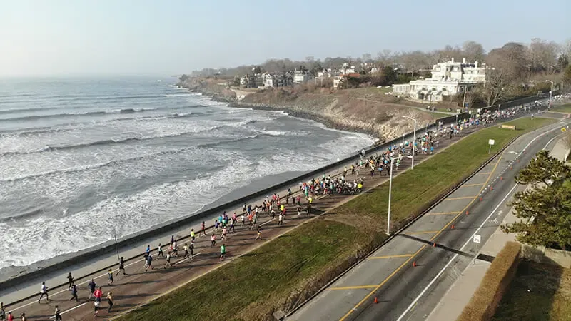 A drone shot of a half marathon with many runners on a road next to the ocean.