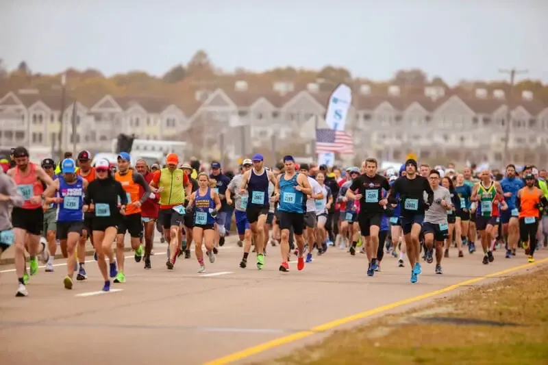 A large group of runners are running down a road during a race, with houses in the background.