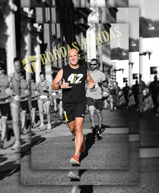 A male runner in a black tank top with '42 RUN' on it, giving a thumbs up and shaka sign while running on a road with other runners in the background.