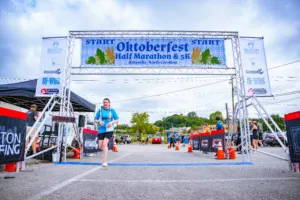 A runner crosses the start line under the Oktoberfest Half Marathon & 5K arch.