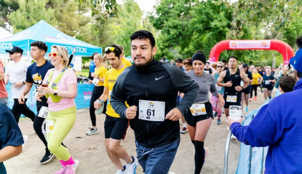 A group of runners starting a race, with a man in the foreground wearing bib number 61.