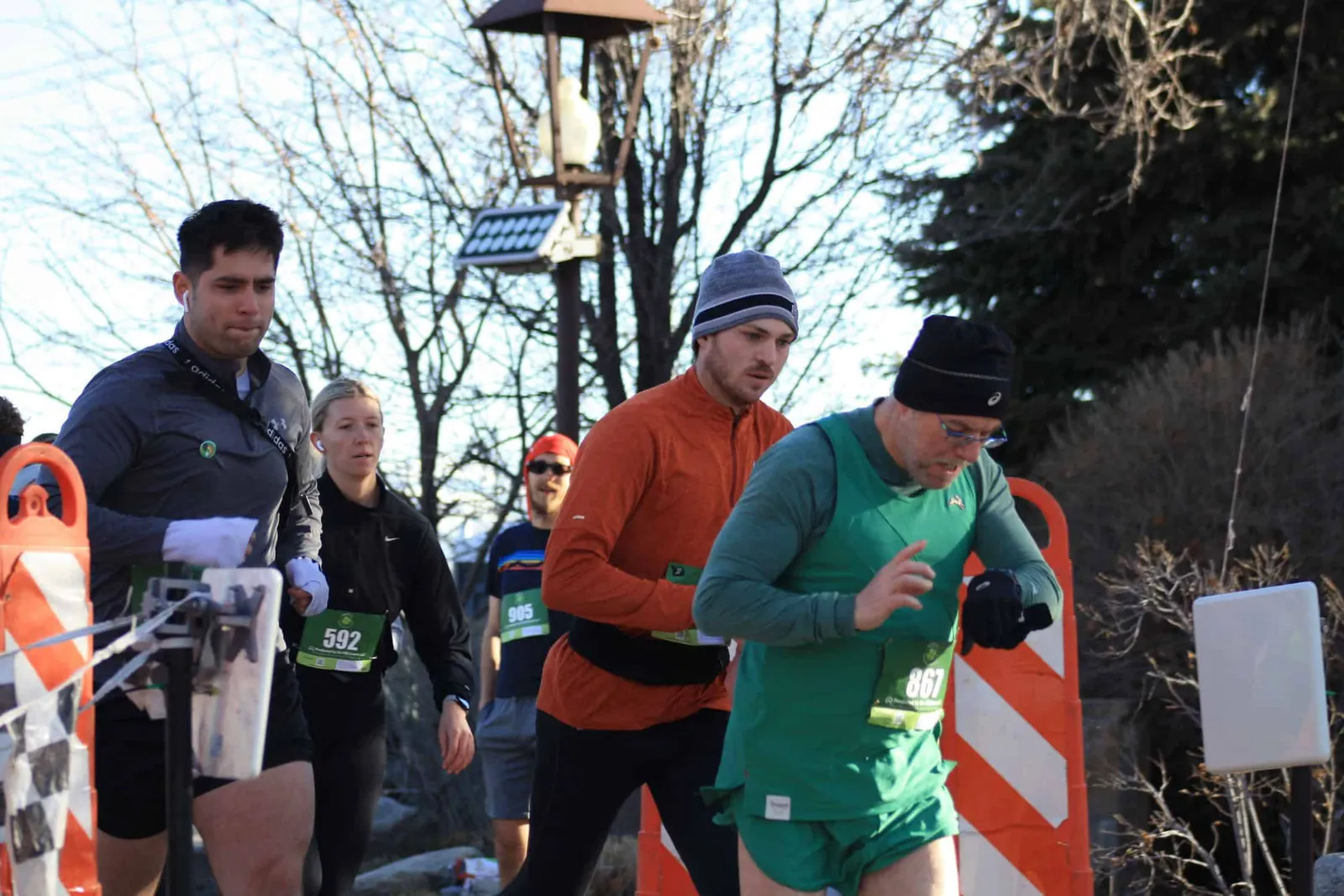 Runners in racing bibs starting a race, with one runner checking his watch.