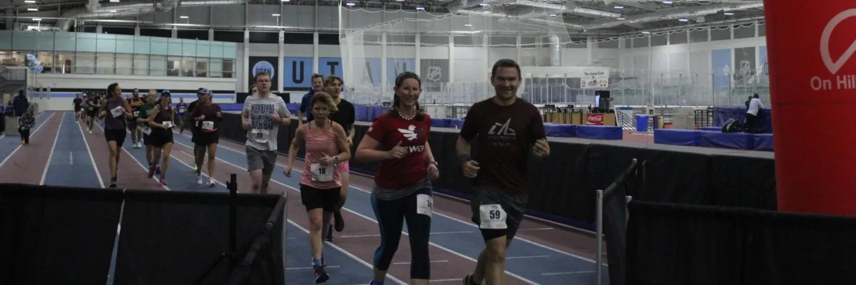 Runners participating in a race on an indoor track, with some smiling and focused.