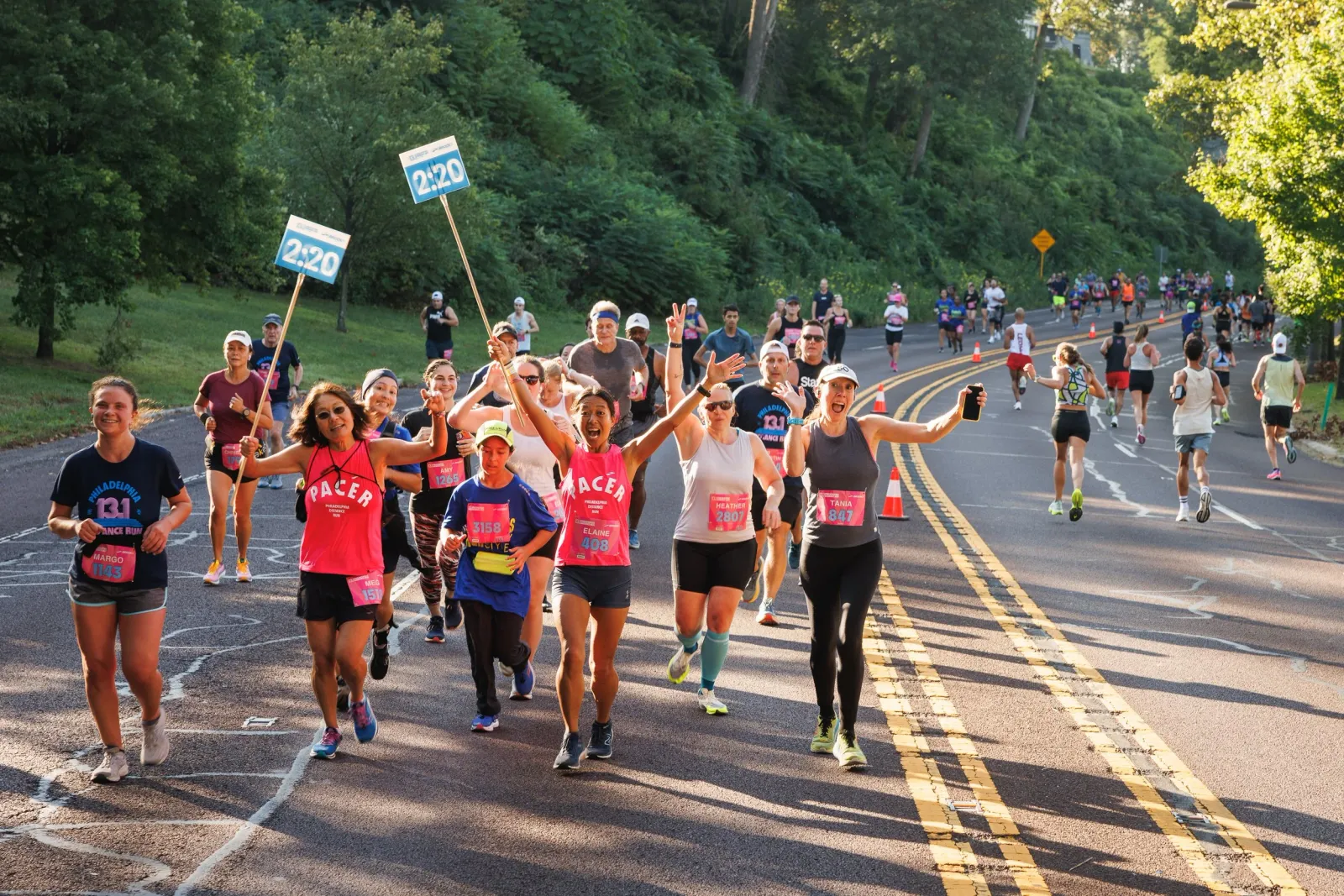 Runners smiling and waving as they participate in a race, with pacers holding '2:20' signs.