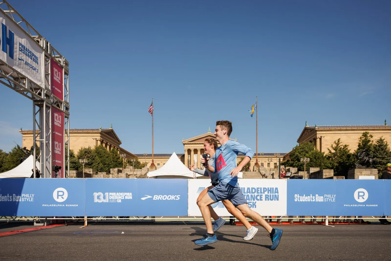 Two runners crossing the finish line at the Philadelphia Distance Run, with the Philadelphia Museum of Art in the background.