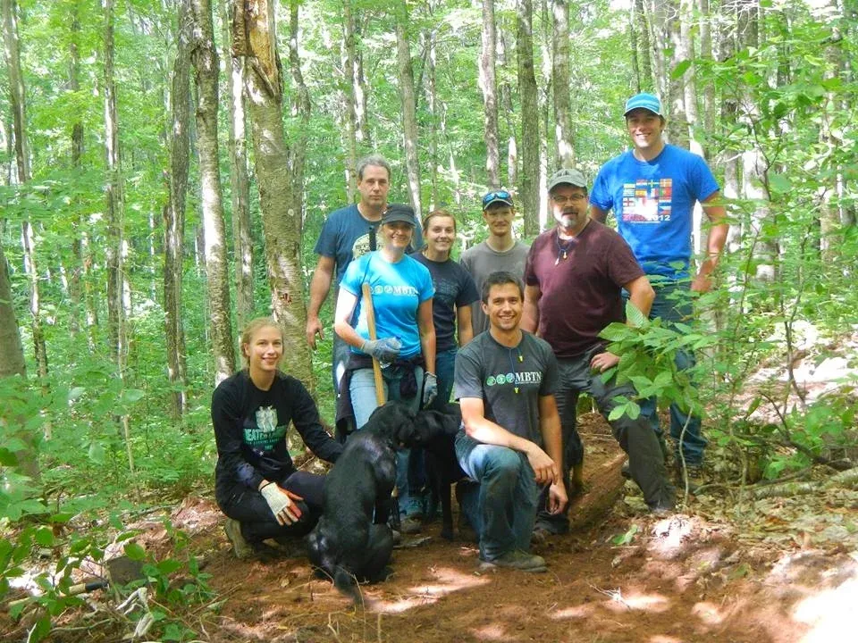 A group of people and a dog posing for a photo in a forest, possibly during trail maintenance or a pre-race event.