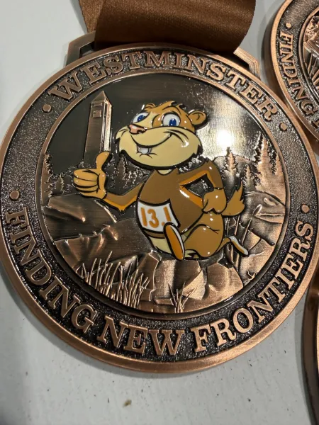 A bronze medal for the Westminster Finding New Frontiers race, featuring a cartoon prairie dog giving a thumbs-up and wearing a bib with the number 13.