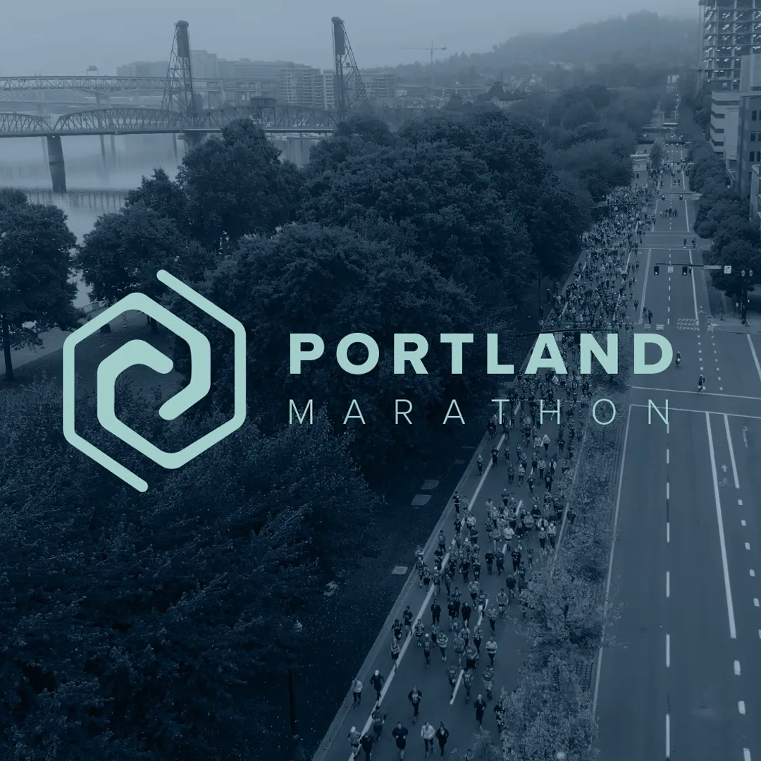 Aerial view of a large crowd of runners participating in the Portland Marathon, with the city skyline and a bridge in the background.