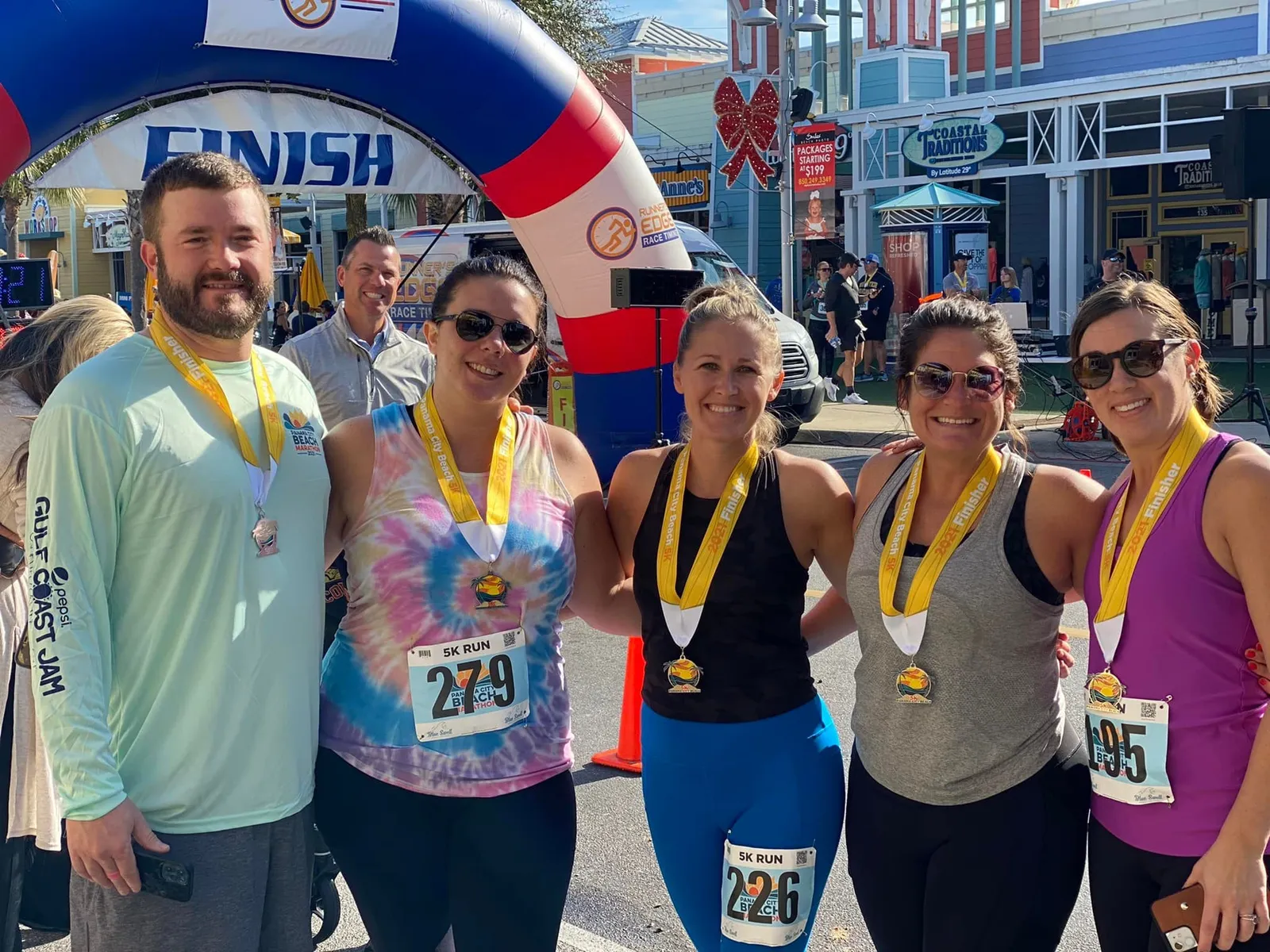 A group of five runners, smiling and posing for a photo after crossing the finish line of the Panama City Beach 5K Run, wearing their finisher medals.