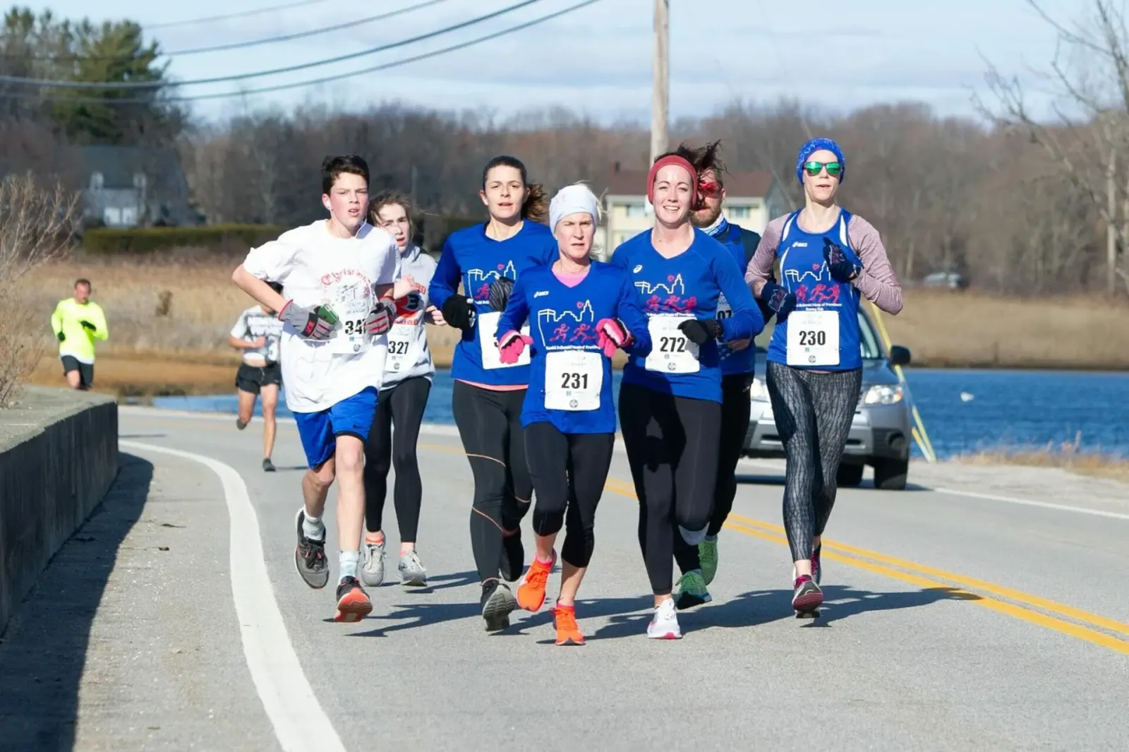 A group of runners, including a young male and several women, running on a road next to a body of water.