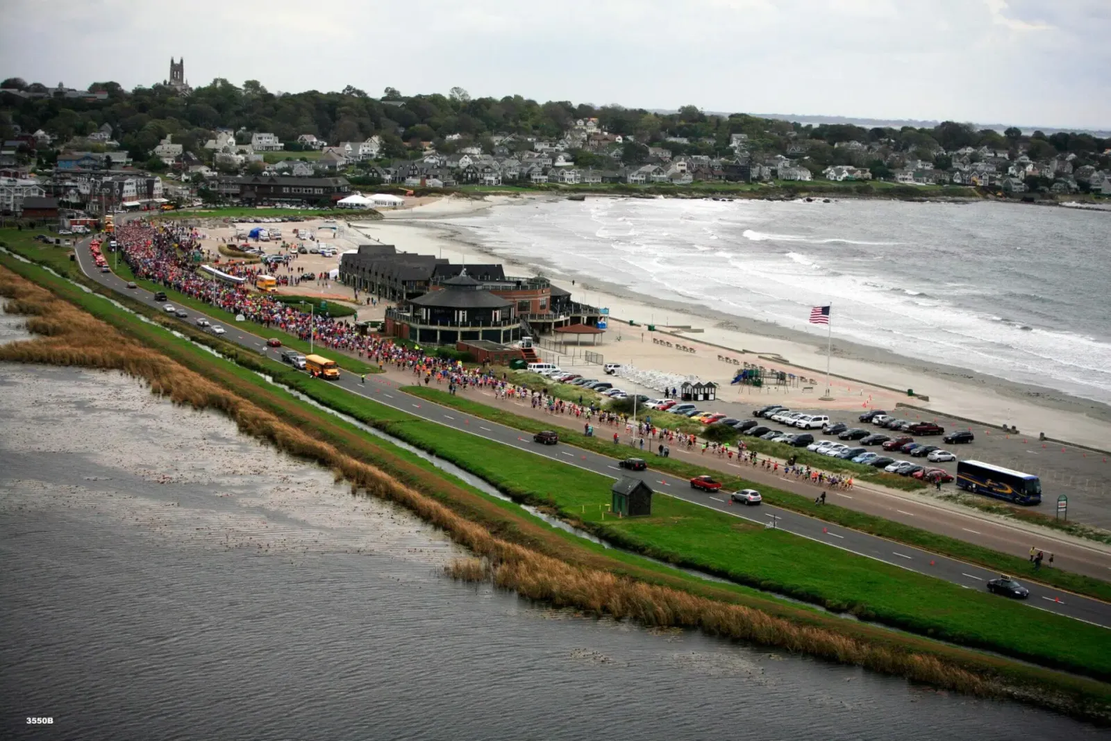 A large group of runners participating in a race along a coastal road with the ocean and beach in the background.