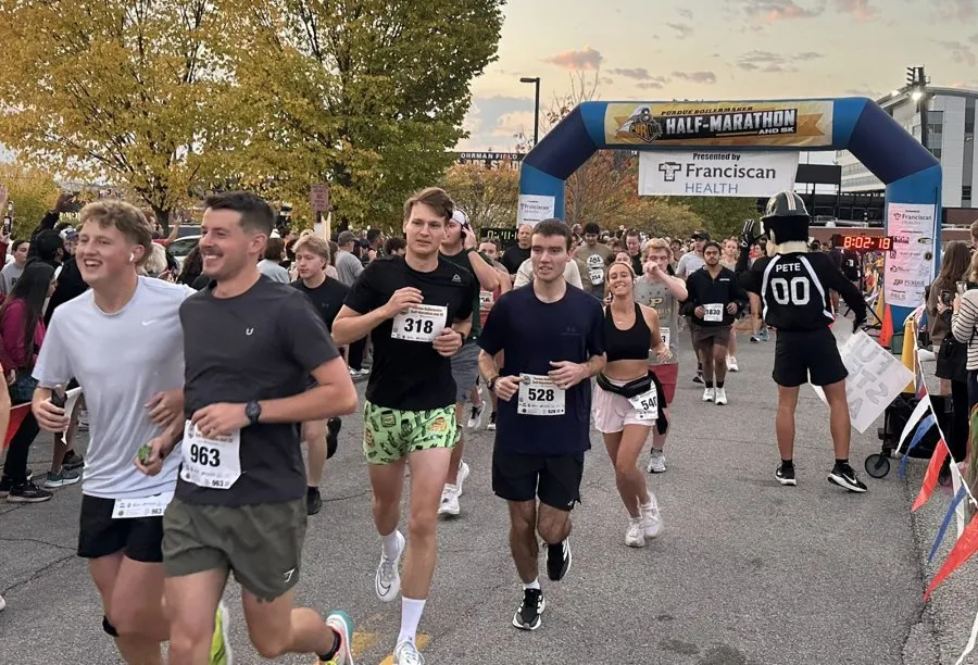 Runners starting the Purdue Boilermaker Half-Marathon and 5K, with an archway and crowd in the background.