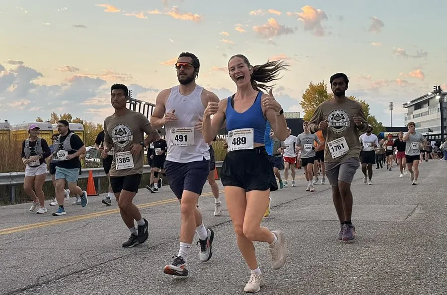 Runners participating in the Purdue Boilermaker Half Marathon and 5K, with a woman in the foreground giving a thumbs-up.