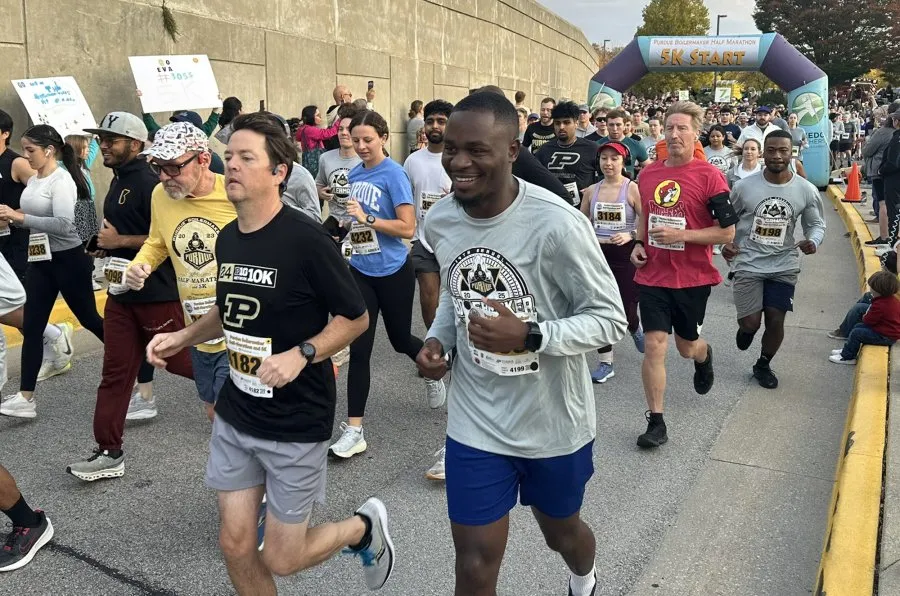 A group of runners are starting the Purdue Boilermaker Half Marathon and 5K, with a large inflatable archway marking the start line.