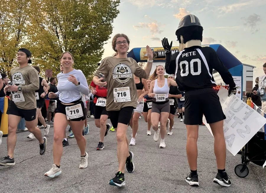Runners high-fiving a mascot at the start line of the Purdue Boilermaker Half Marathon & 5K.