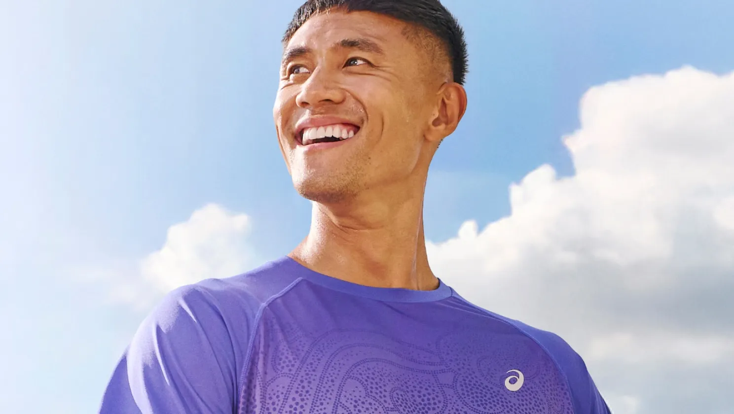 A smiling man in a purple running shirt looks up at the sky.