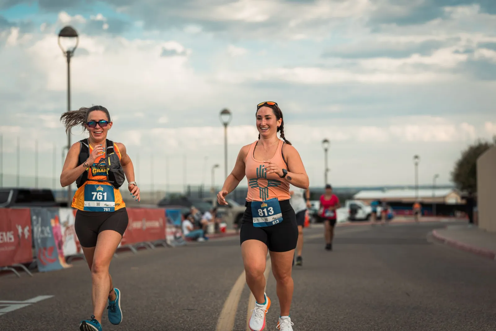 Two female runners smiling as they run down a road during a race.