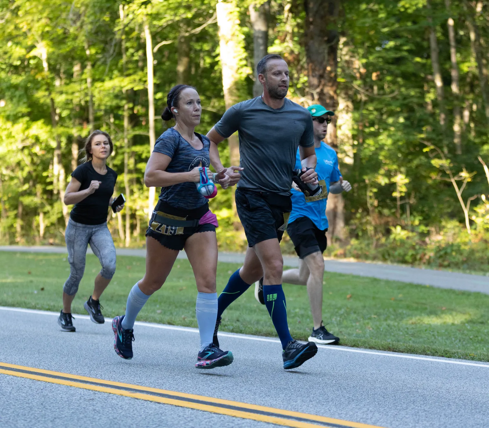 Runners on a paved road with a forest on the side.