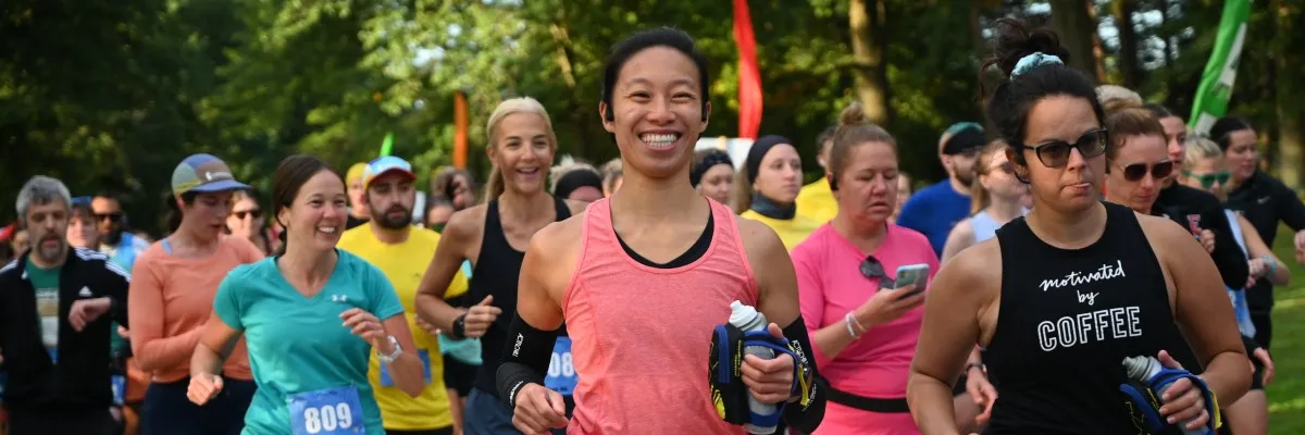 A diverse group of runners participating in a race, with a smiling woman in a pink tank top in the foreground.