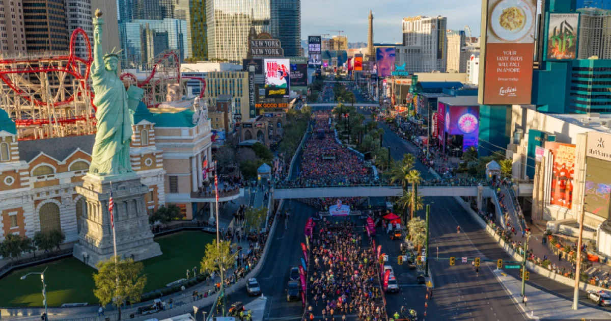 A massive crowd of runners participating in a marathon on the Las Vegas Strip, with the Statue of Liberty replica and towering casinos in the background.
