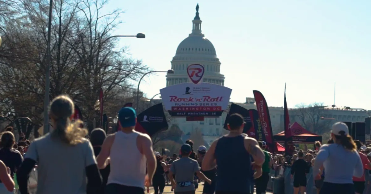 Runners approaching a large Rock 'n' Roll Running Series banner with the U.S. Capitol building in the background.
