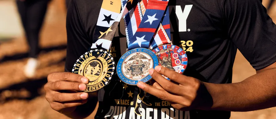 A runner holds up multiple finisher medals, with one medal prominently displaying 'ITALIAN STALLION CHALLENGE 2024'.