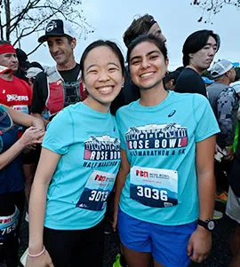 Two young women smiling at the camera, wearing Rose Bowl Half Marathon & 5K t-shirts and bibs.