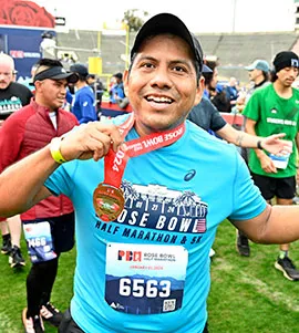 A smiling runner proudly displays his Rose Bowl Half Marathon & 5K medal.
