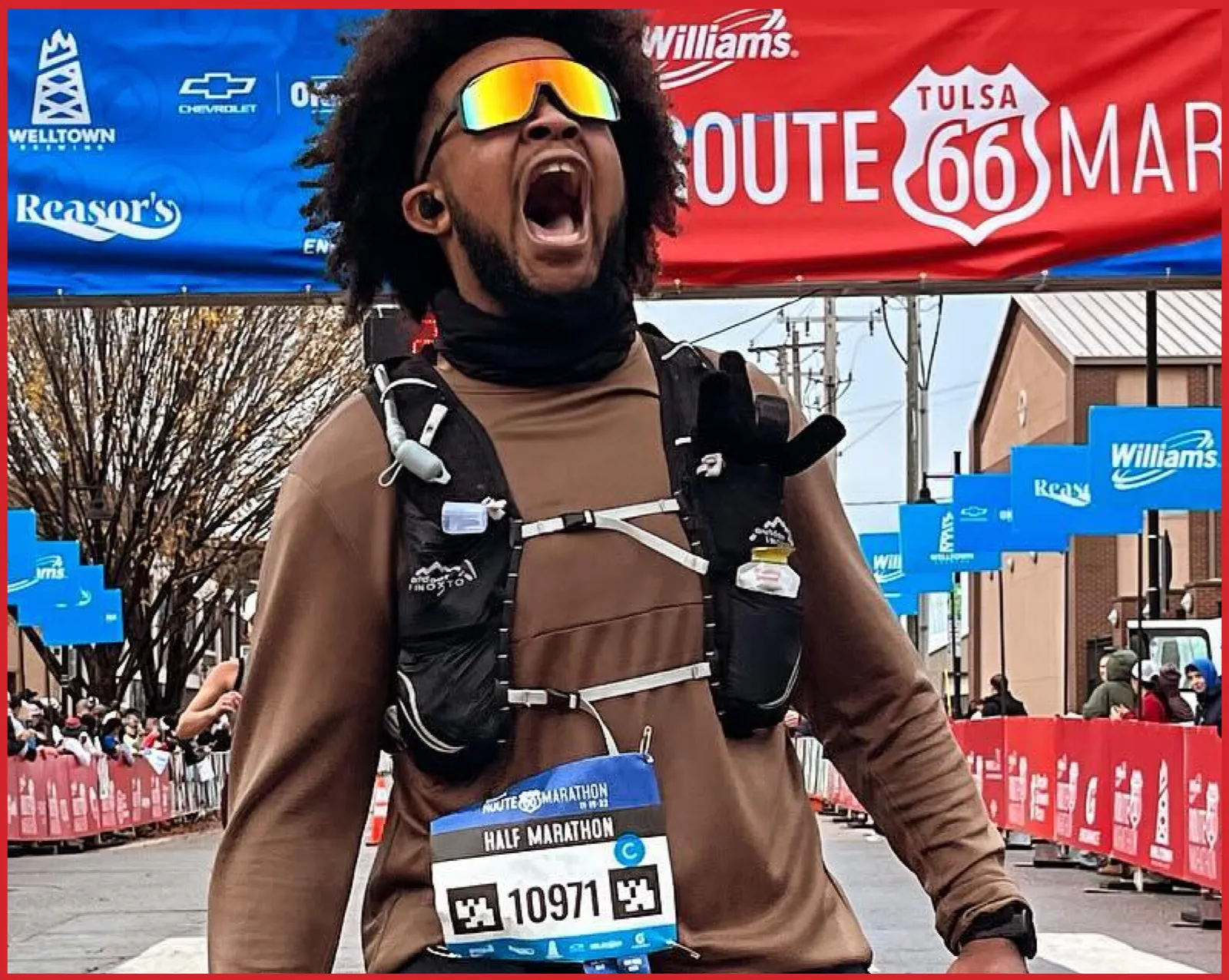 A runner with an ecstatic expression, wearing sunglasses and a bib for the Route 66 Half Marathon, crosses the finish line.