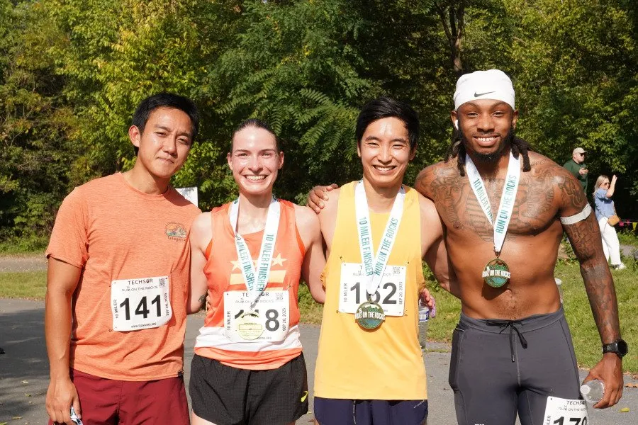 Four runners, two men and two women, pose for a photo after a race, all wearing medals and smiling.