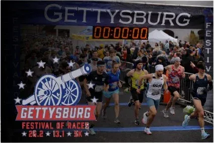 Runners starting the Gettysburg Festival of Races with a large crowd in the background and the race logo prominently displayed.
