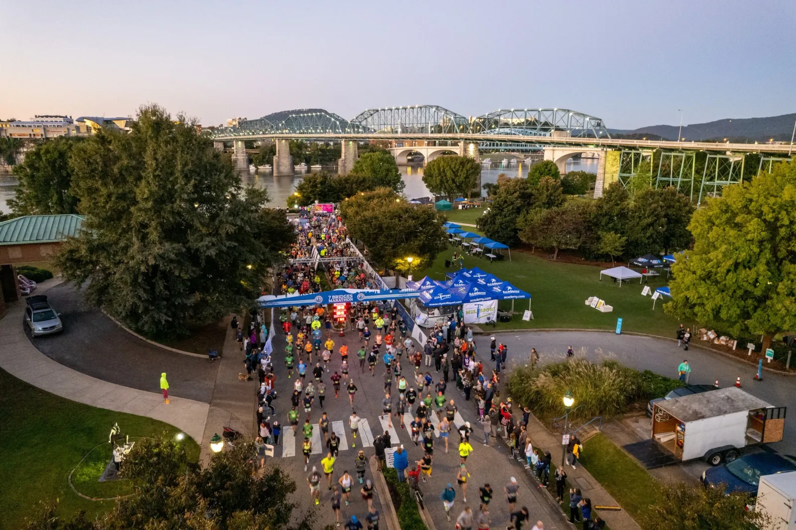 Runners crossing the start line of the 7 Bridges Marathon with large bridges in the background.
