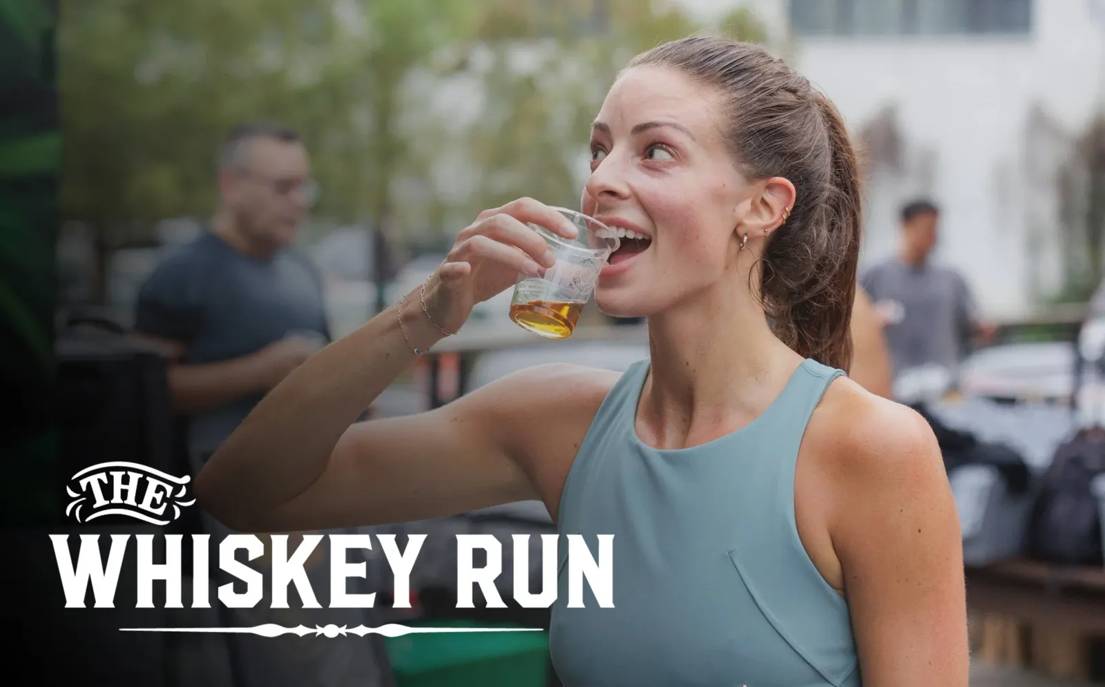 A woman smiles as she drinks from a small cup, with the words "THE WHISKEY RUN" overlaid on the image.