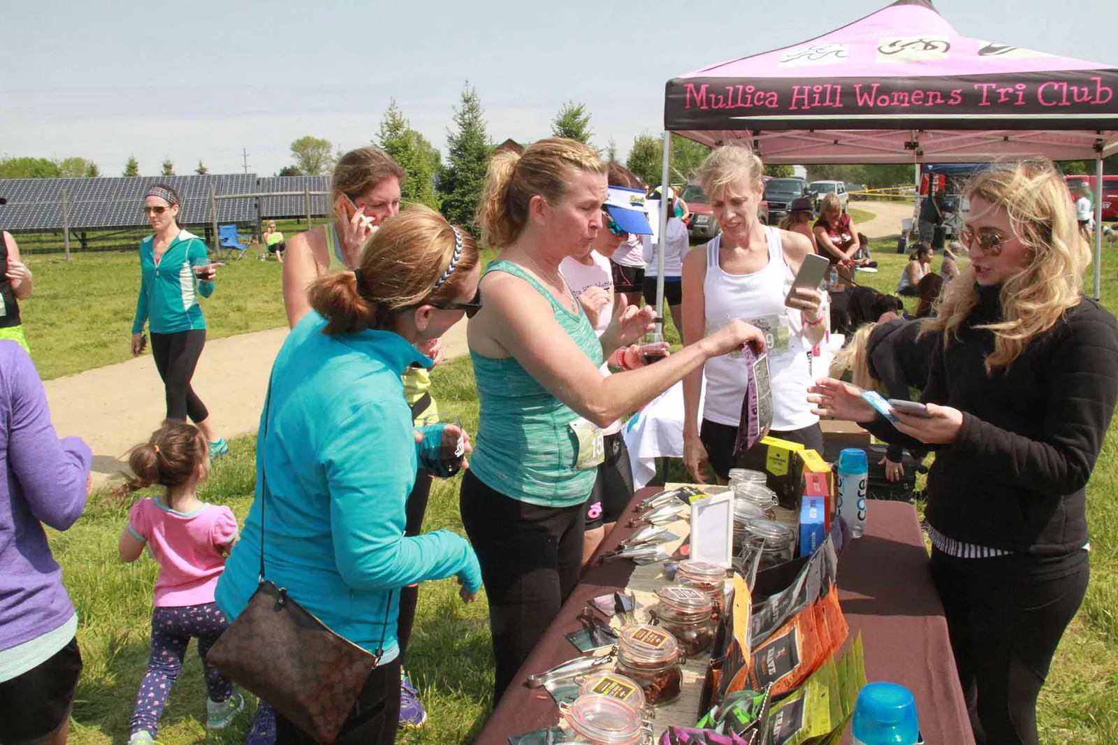 People gathered around a table at an outdoor event, with a pink tent in the background.
