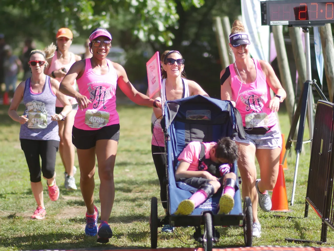 Runners in pink racing tops crossing a finish line, one pushing a stroller with a sleeping child.