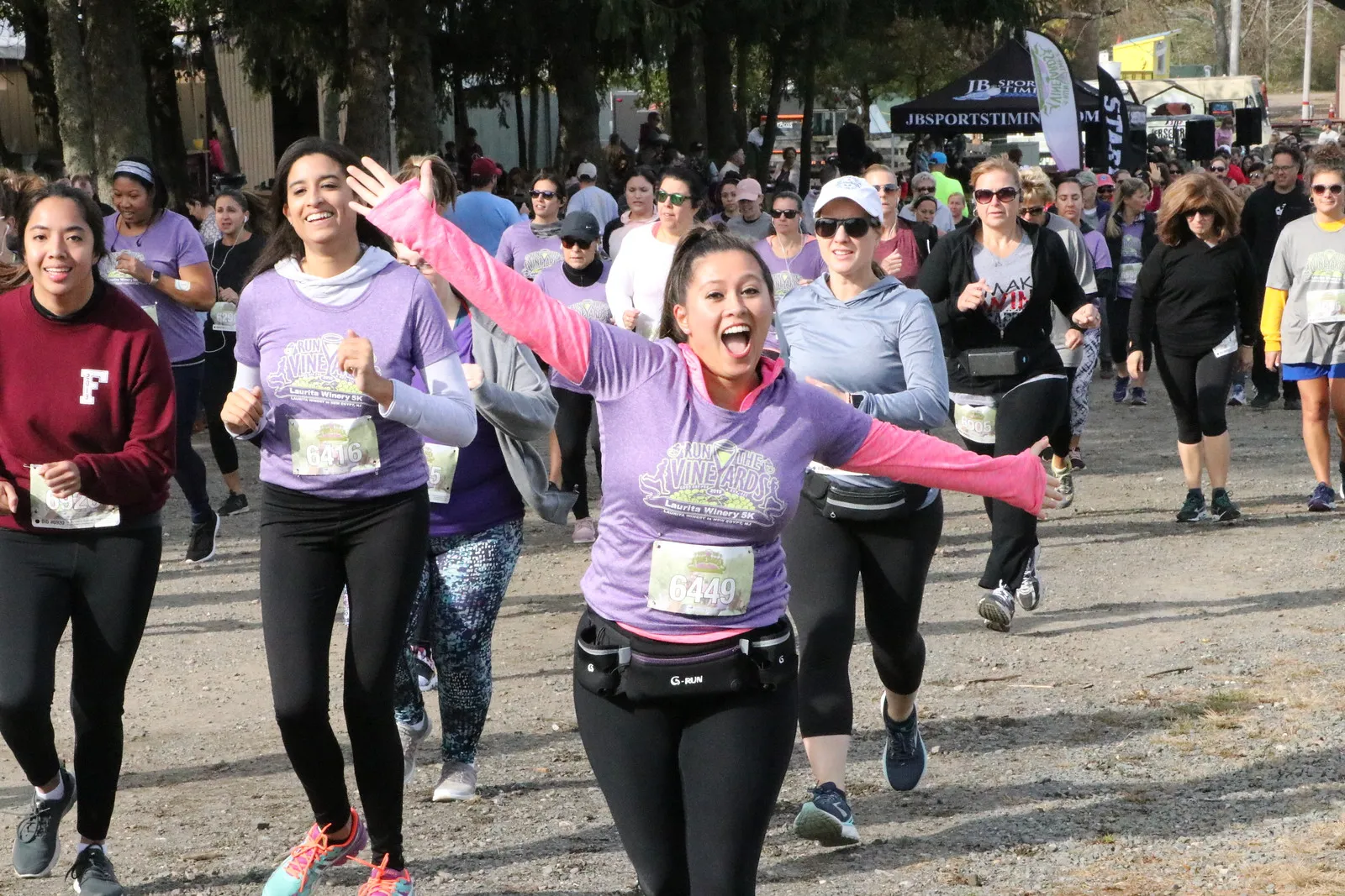 A group of female runners smiling and cheering as they start a race, with one runner in the foreground with arms outstretched.