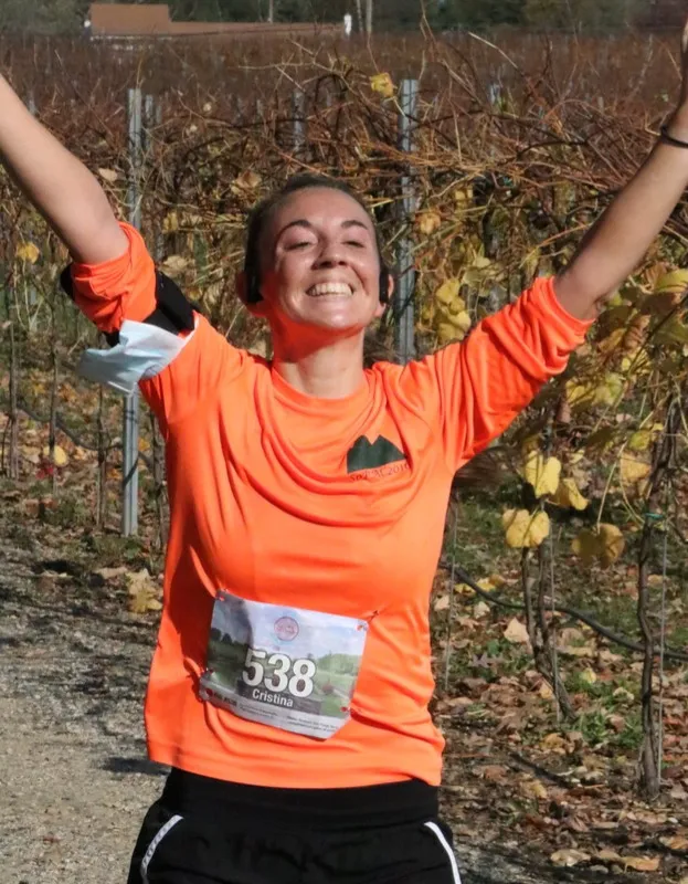 A female runner in an orange shirt with her arms raised in celebration, wearing bib number 538.